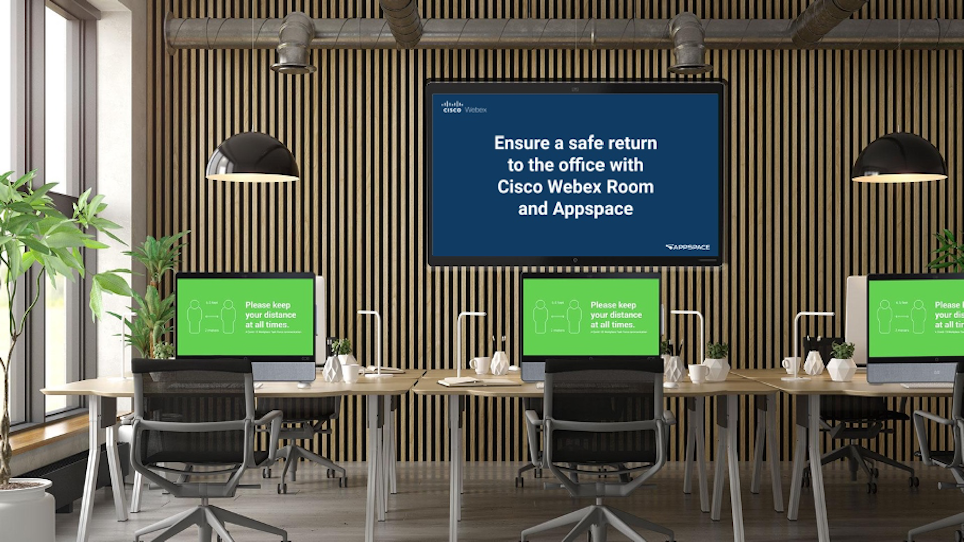 A modern office space with wooden paneling and plants, featuring a screen displaying a message about returning safely with Cisco Webex Room and Appspace. Desks have green signs that read, Please keep your distance at all times.
