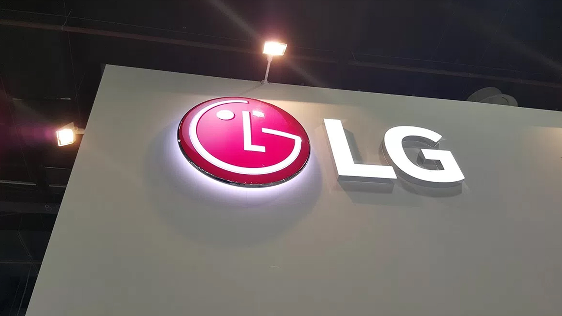 A wall featuring the LG logo: a large, illuminated red circle with a stylized white L and G forming a face. Next to it, the letters LG appear in white. The setting is likely an indoor event or exhibition.