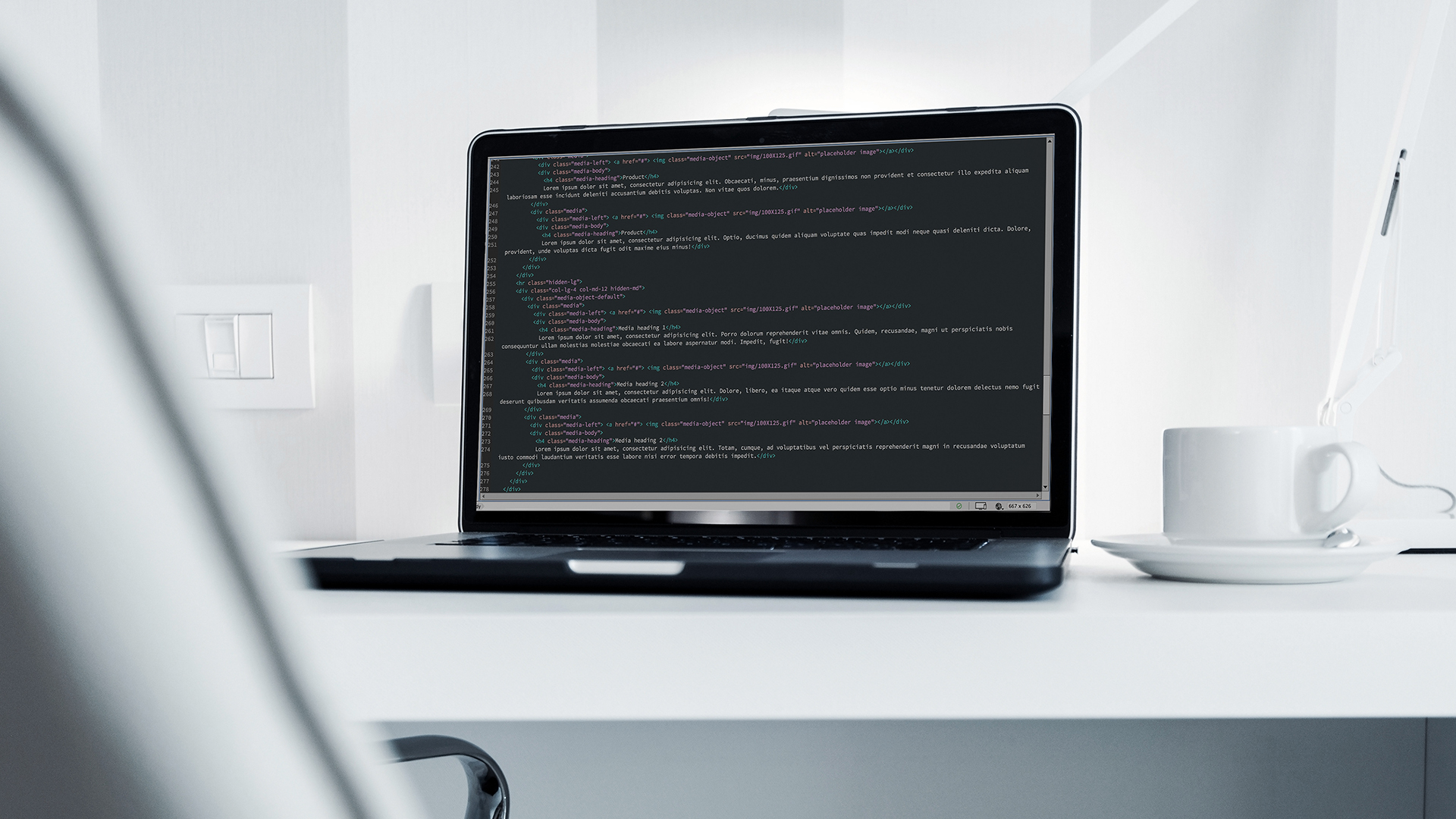 A laptop displaying HTML code on its screen is placed on a white desk. Beside the laptop, theres a white coffee cup and a lamp. The background shows a wall socket and blurred vertical stripes on the wall.