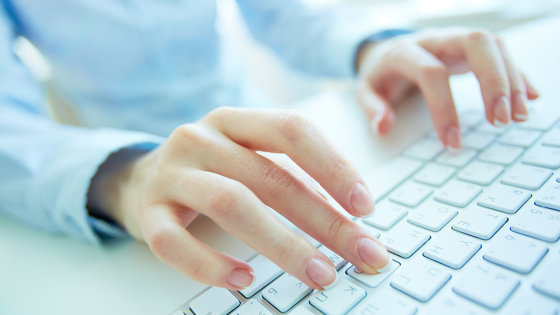 A close-up of hands typing on a white keyboard, with a blurred background.