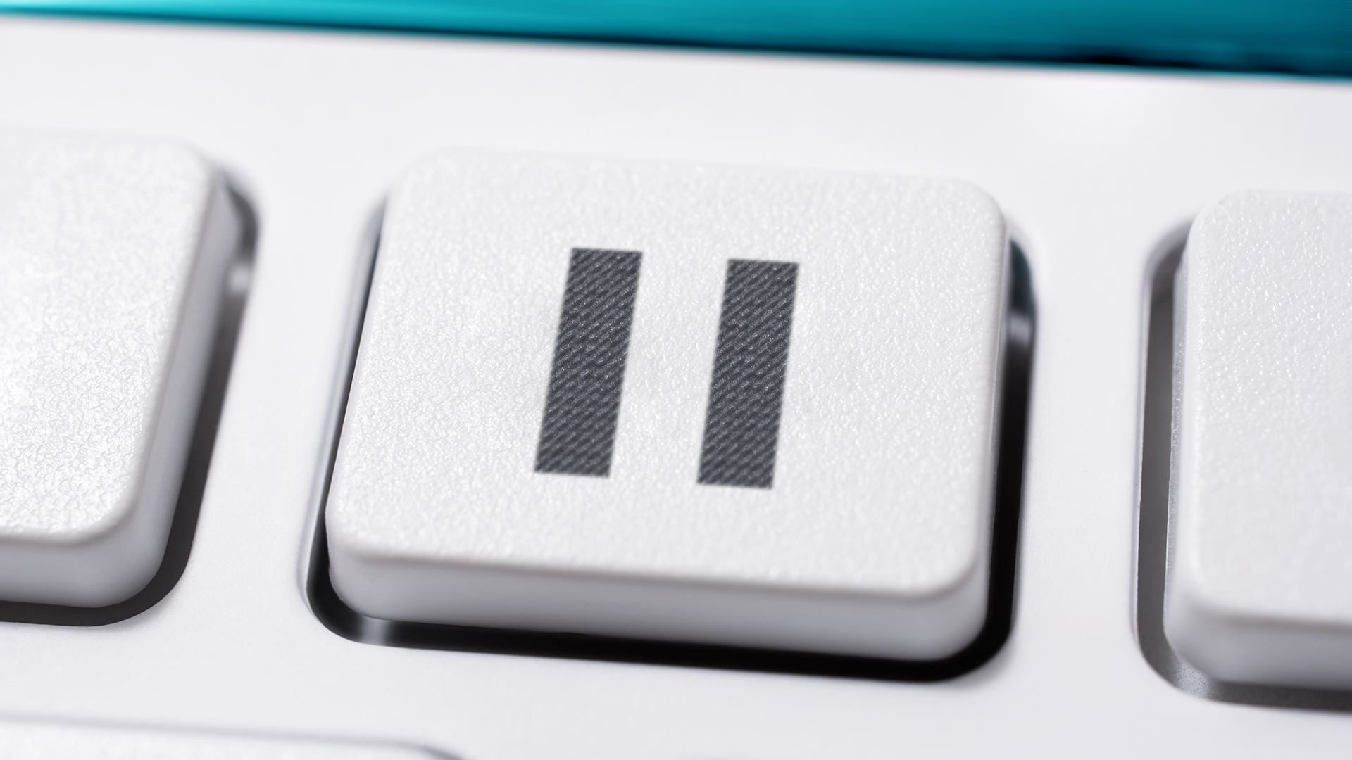 Close-up image of a keyboard key featuring the pause symbol, represented by two vertical bars. The key is white with a textured surface, and part of the adjacent keys are visible.