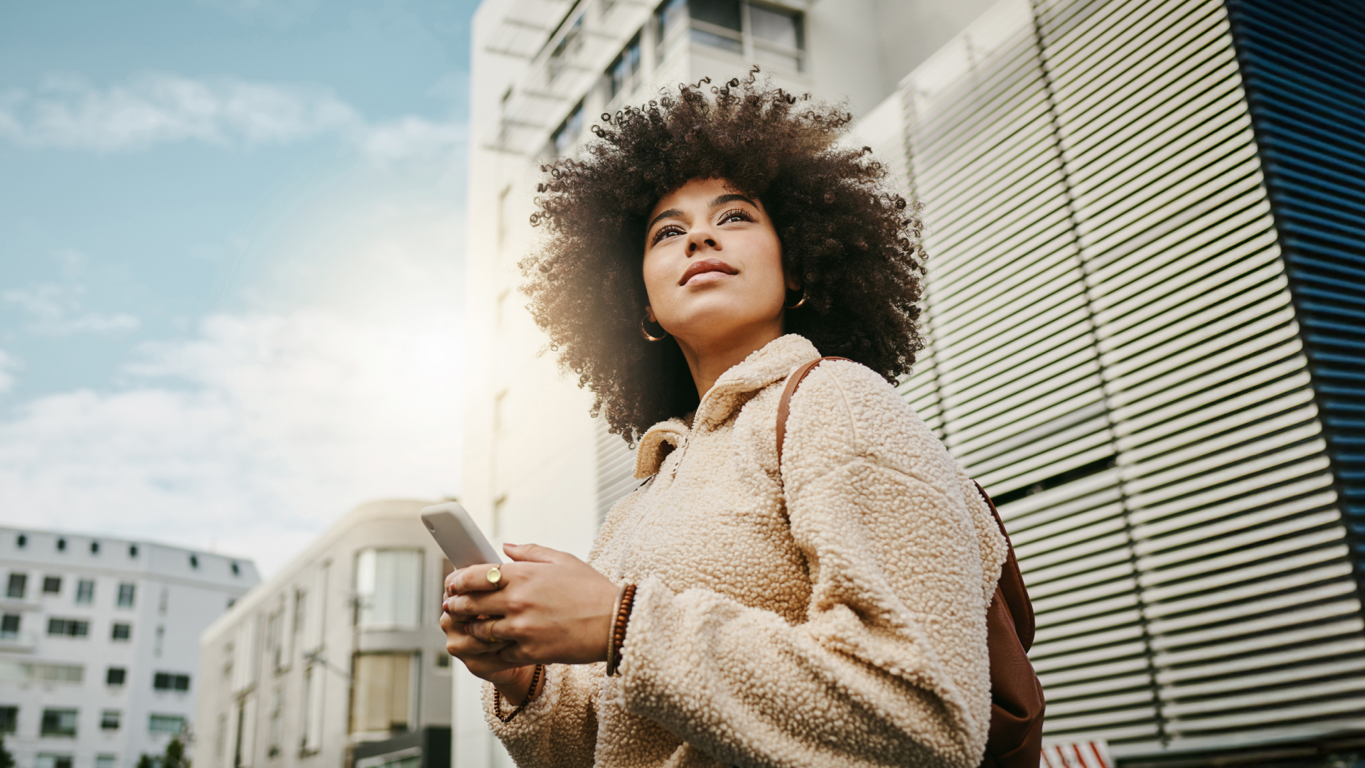 Young professional looking up thoughtfully while holding a phone, symbolizing workplace disconnection and the need for better communication tools.