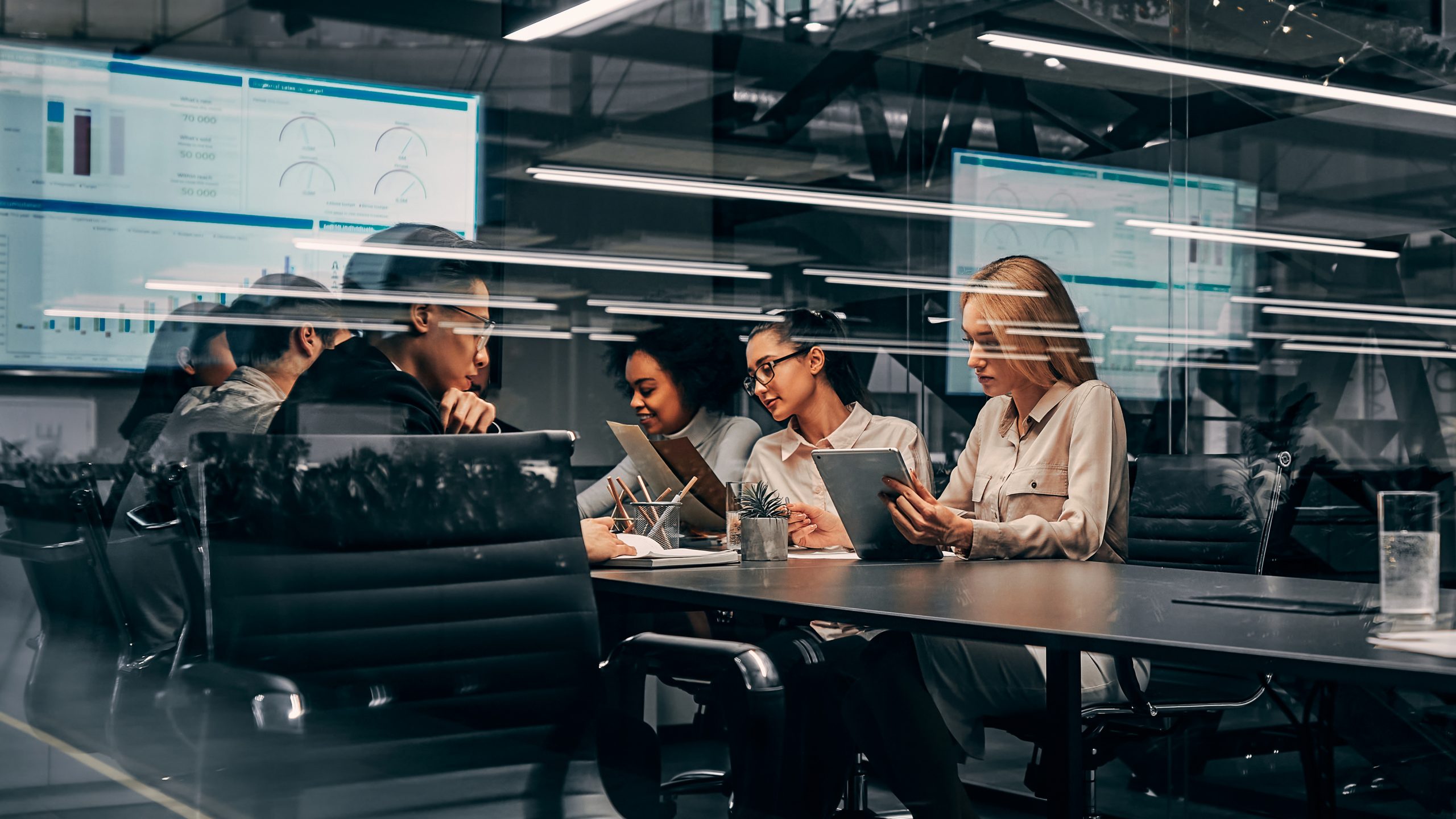 Modern business. Young focused serious business women and men working in a conference room working on a project presentation. Light from a spacious office is reflected through the glass.