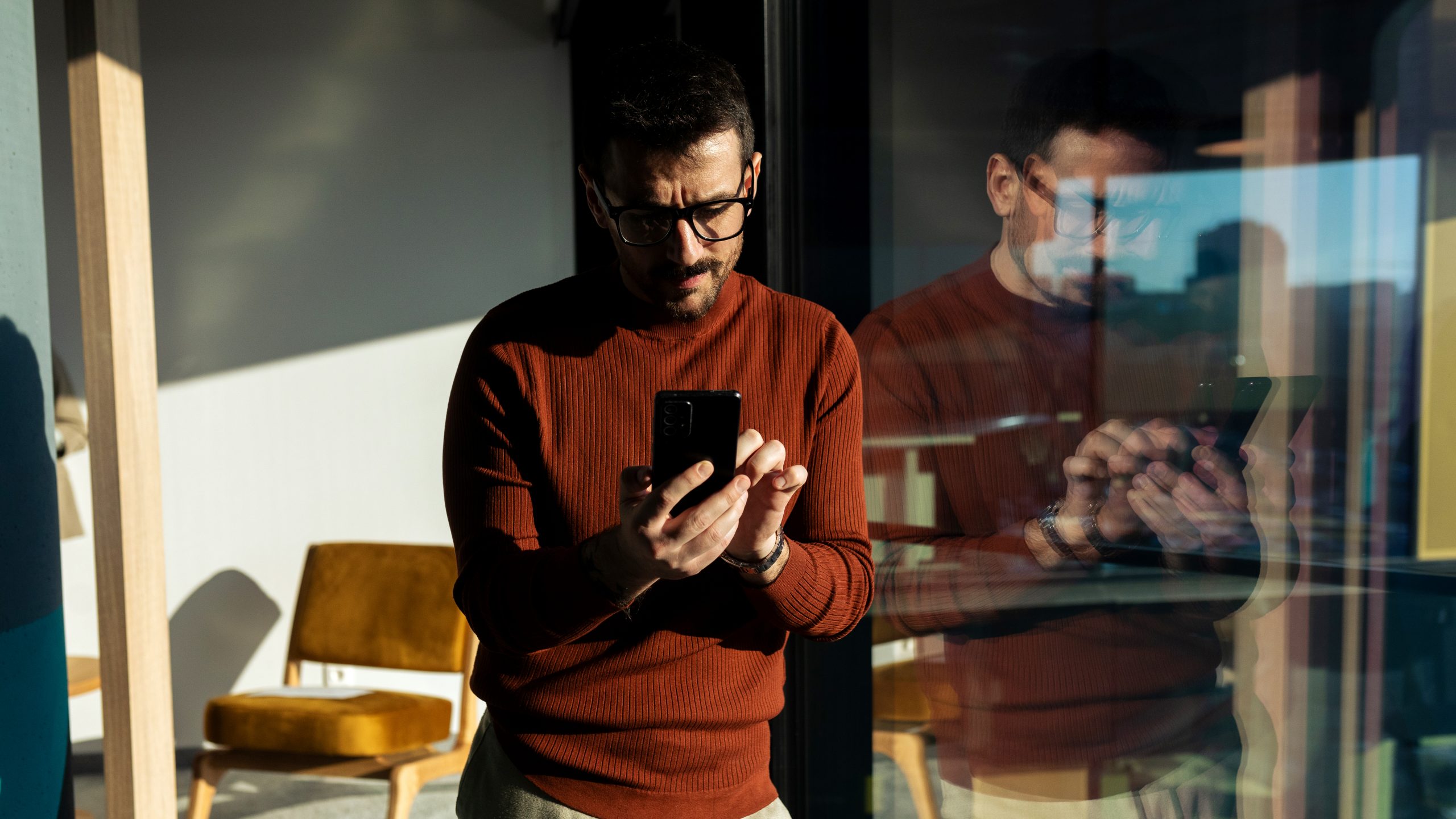 Mid adult man using his phone next to the office window