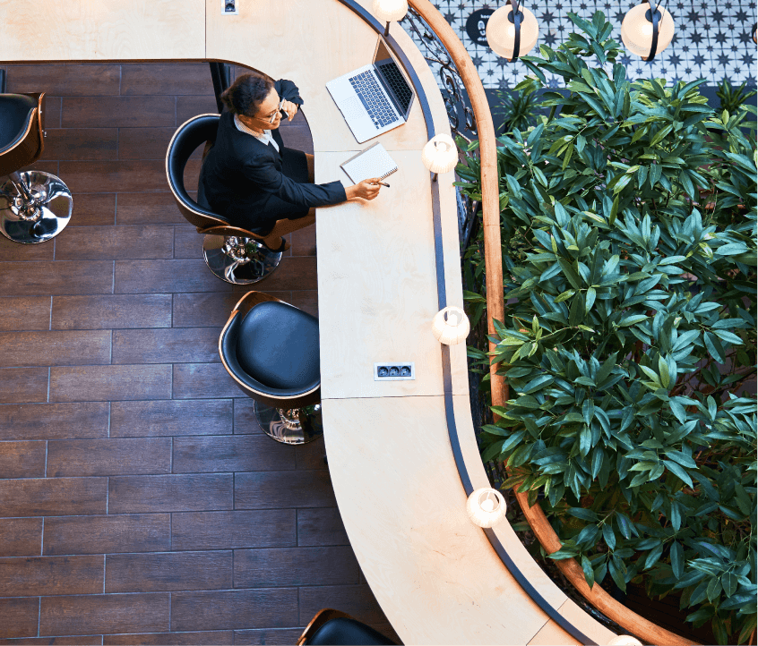Aerial view of a professional woman working in a common area with lush greenery.