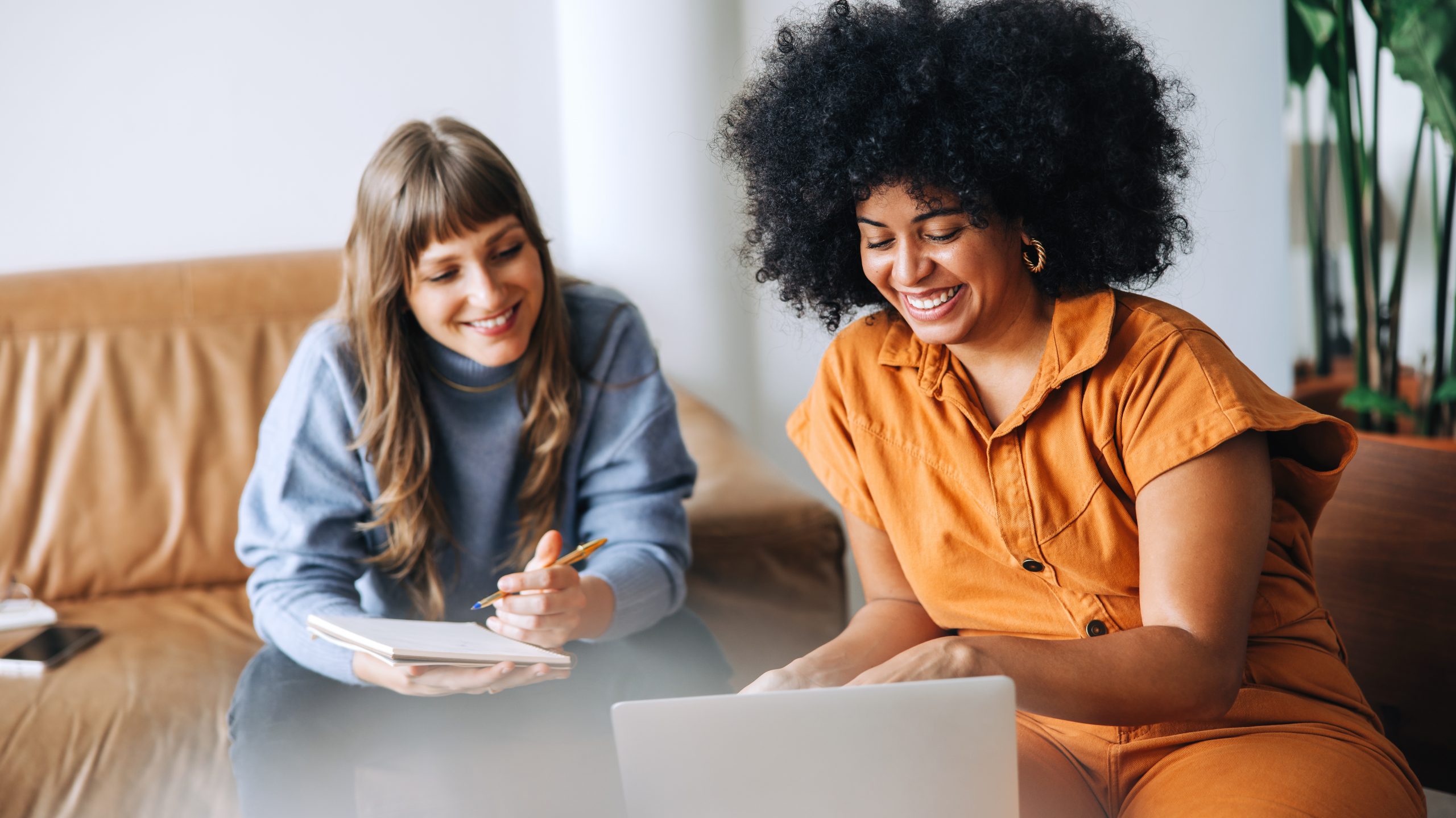two work colleagues smile as they collaborate and read work communications on a laptop