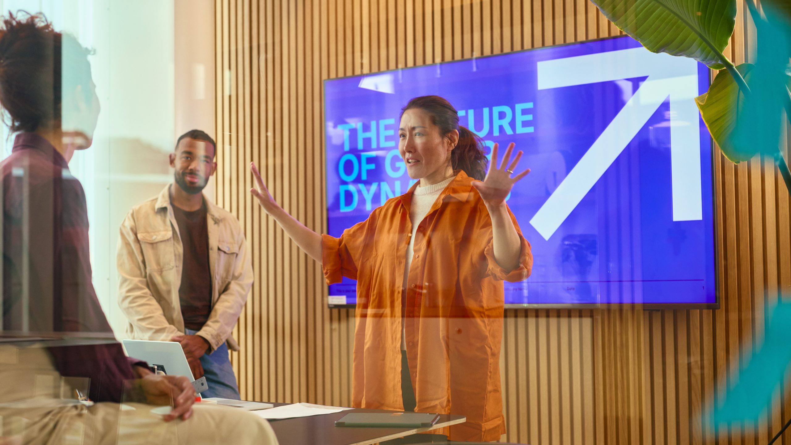 Business team working in a modern office, in front of a digital signage display, connecting in office, frontline and remote employees with the same messaging.